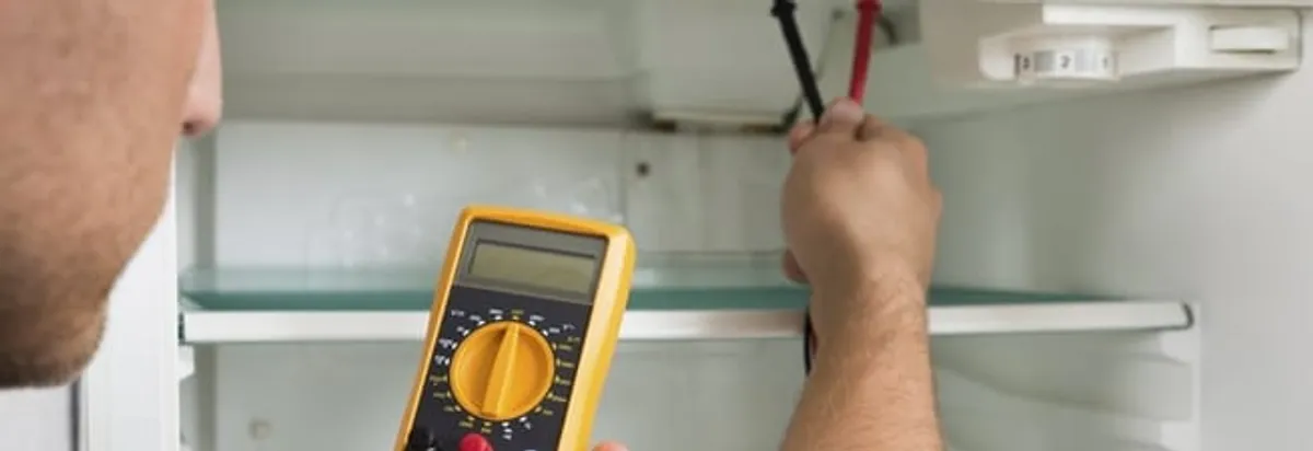 Refrigerator repair technician testing electrical components with a multimeter in Columbia, MO